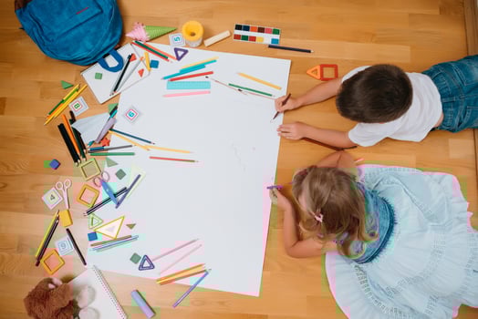 Kids drawing on floor on paper. Preschool boy and girl play on floor with educational toys - blocks, train, railroad, plane. Toys for preschool and kindergarten. Children at home or daycare. Top view. photo