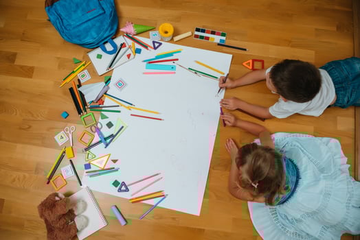 Kids drawing on floor on paper. Preschool boy and girl play on floor with educational toys - blocks, train, railroad, plane. Toys for preschool and kindergarten. Children at home or daycare. Top view. photo