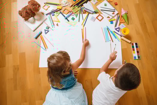Kids drawing on floor on paper. Preschool boy and girl play on floor with educational toys - blocks, train, railroad, plane. Toys for preschool and kindergarten. Children at home or daycare. Top view. photo