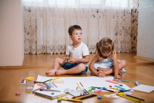 Kids drawing on floor on paper. Preschool boy and girl play on floor with educational toys - blocks, train, railroad, plane. Toys for preschool and kindergarten. Children at home or daycare photo