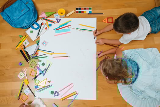 Kids drawing on floor on paper. Preschool boy and girl play on floor with educational toys - blocks, train, railroad, plane. Toys for preschool and kindergarten. Children at home or daycare. Top view. photo