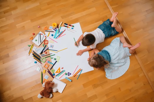 Kids drawing on floor on paper. Preschool boy and girl play on floor with educational toys - blocks, train, railroad, plane. Toys for preschool and kindergarten. Children at home or daycare. Top view. photo