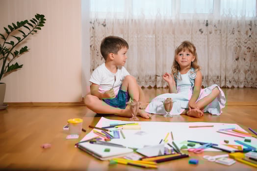 Kids drawing on floor on paper. Preschool boy and girl play on floor with educational toys - blocks, train, railroad, plane. Toys for preschool and kindergarten. Children at home or daycare. photo