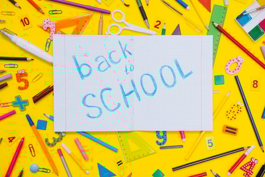 School notebook and stationery over yellow desk. Back to school abstract background. School equipment. Variety of school supplies. Flat lay photo