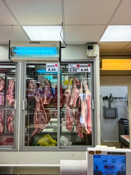 Budva, Montenegro - 17 august 2023. Glass showcases of a refrigerator with hanging meat carcasses on hooks photo