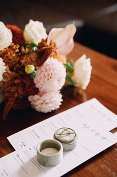 Engagement ring in a box stands on a festive menu on a wooden table near a bouquet photo