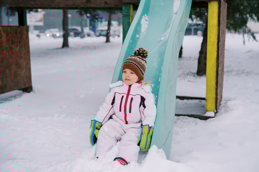 Little girl sliding down a snow-covered colorful slide photo