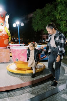 Mom helps a little girl go down from the cup-shaped carousel holding her hand photo