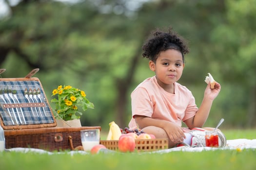 Happy family enjoying a picnic in the park, with kid eating jam bread, surrounded by nature photo