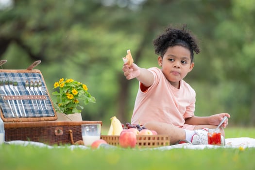 Happy family enjoying a picnic in the park, with kid eating jam bread, surrounded by nature photo