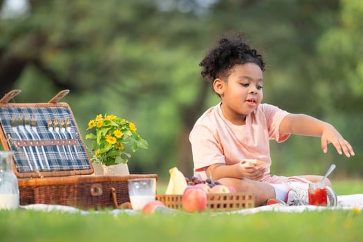 Happy family enjoying a picnic in the park, with kid eating jam bread, surrounded by nature photo