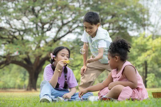 Children sitting in the park with blowing air bubble, Surrounded by greenery and nature photo