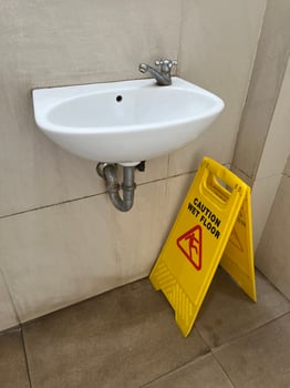 Caution wet floor yellow warning board under the sink with blue floor dryer in public toilet photo