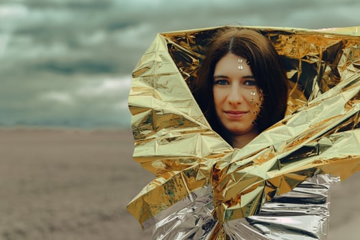 woman is standing on a road wearing a silver and gold rescue blanket photo