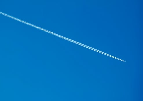 Airplane condensation trail and airplane on blue sky photo
