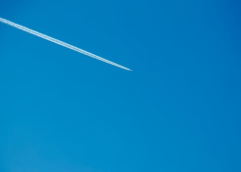 Airplane condensation trail and airplane on blue sky photo