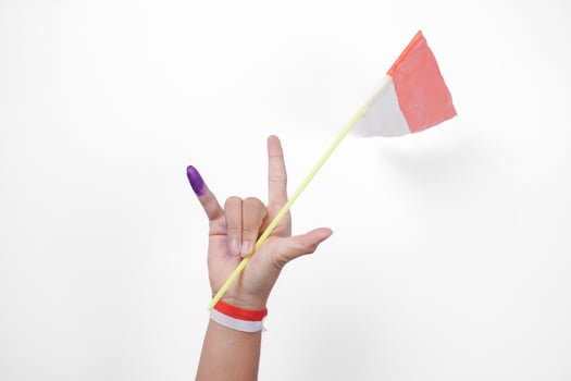Group of hand wearing flag ribbon on wrist showing little finger dipped in purple ink after voting for Indonesia Election or Pemilu while holding mini flag, isolated over white background photo