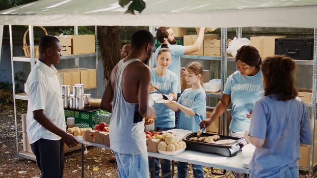 Caucasian girl volunteering by handing out free food to needy at non-profit food drive event. Group of volunteers providing humanitarian aid to homeless people and those in poverty. Aerial, handheld. photo