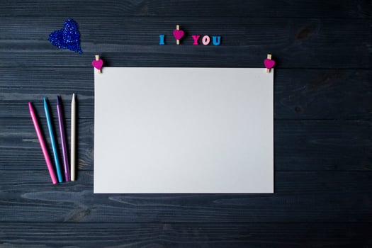 White paper, colorful pencils and decor on a blue wooden background. Greeting card photo