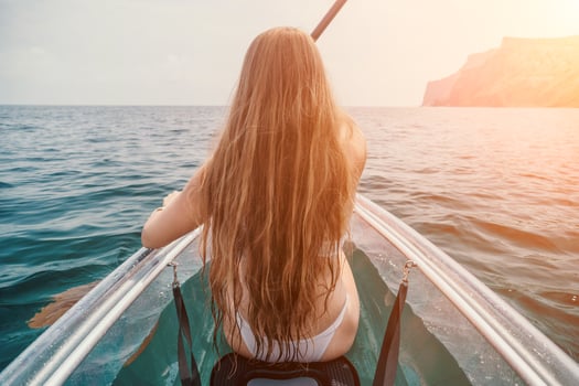 Woman in kayak back view. Happy young woman with long hair floating in transparent kayak on the crystal clear sea. Summer holiday vacation and cheerful female people relaxing having fun on the boat photo