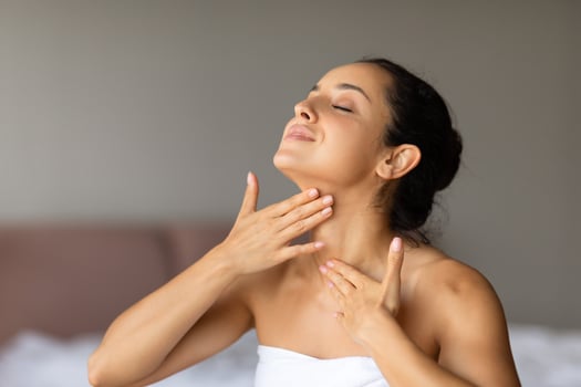 Happy caucasian lady applies moisturizer massaging neck at bedroom photo