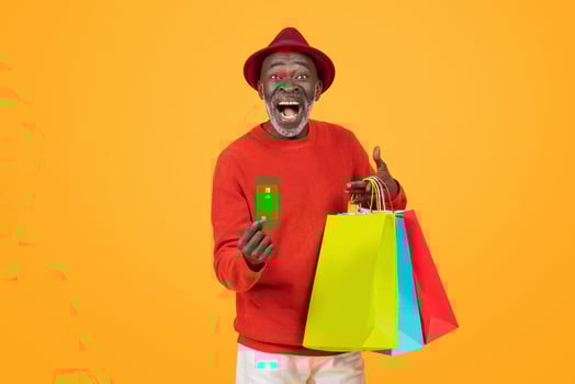 Joyful elderly black man in a vibrant red hat and sweater, holding a credit card photo