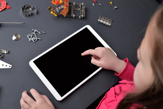 Little girl uses a tablet on a desk, surrounded by small parts and screws. The concept of education and composition of subjects, programming for children photo