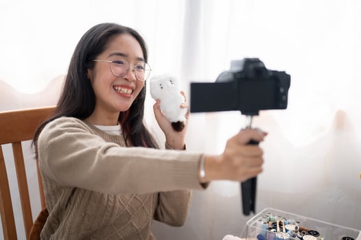 A smiling Asian female content creator is talking with the camera, showing her handmade plushie. photo