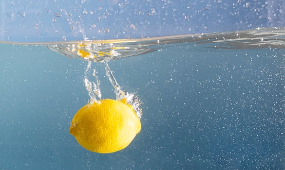 Fresh lemon soaked deep into the splashing blue water. Blue pool water and a fruit motion. Creative summer food concept. photo