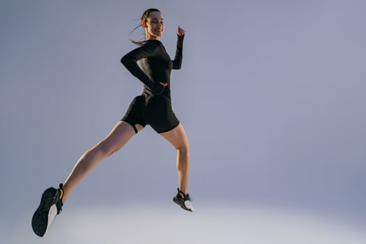 Smiling sporty woman running in Mid-Air exercising during cardio workout over studio background photo