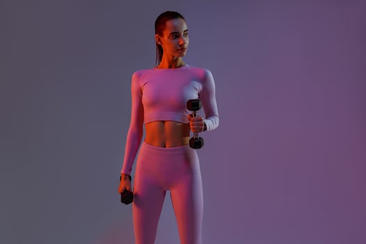 Attractive fitness woman doing exercises with dumbbells on studio background and looking at side photo