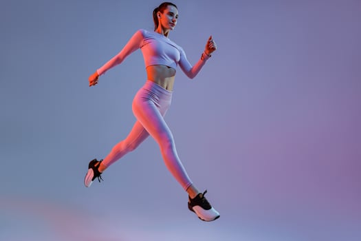 Determined sporty woman running in Mid-Air exercising during cardio workout over studio background photo