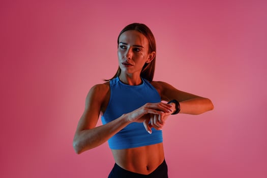 Sporty woman standing and looking at smartwatch checking her performance on studio background photo