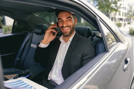 Smiling businessman talking phone with client while sitting on car backseats photo