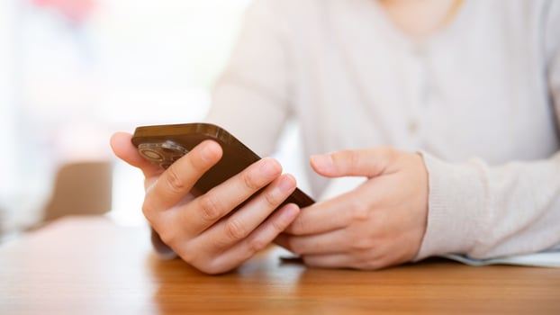 A cropped shot of an Asian woman using her smartphone at a table in a cosy coffee shop. photo