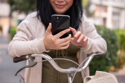 A beautiful, happy young Asian woman in a cute dress is using her smartphone on her bike in the city photo