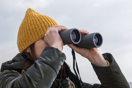 female ornithologist birdman watches birds with binoculars on dirt gravel road against a background of a stormy sky photo