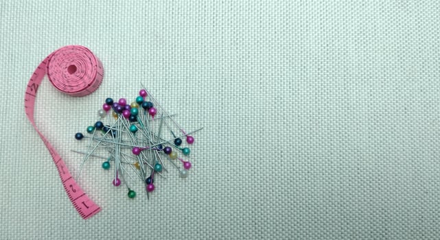 sewing needles and pins of different colors, ruler on white cloth background photo