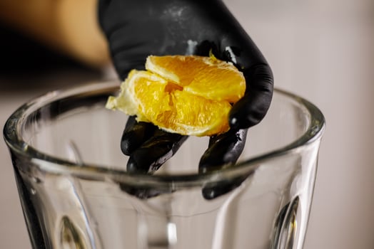 Person with black gloves putting peeled orange half into blender photo