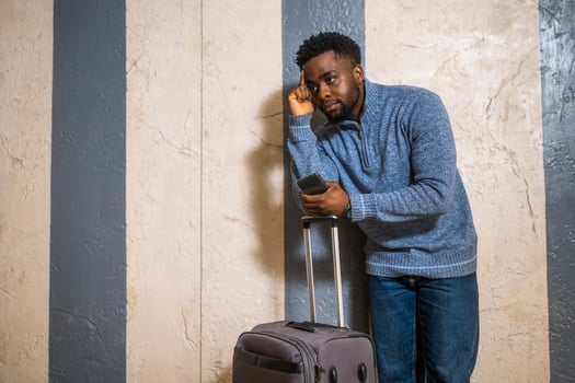 Worried man with suitcase and mobile phone leaning against a wall in passage of the railway station. Copy space on image for your advert or text. photo