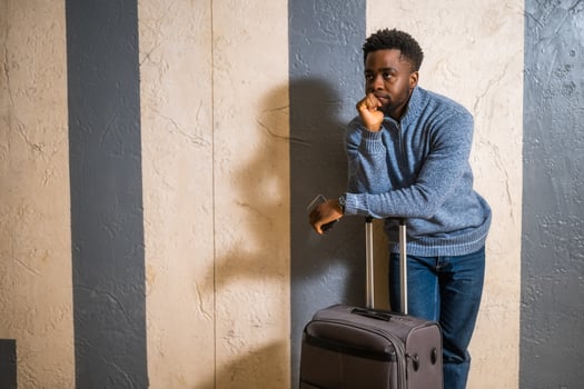 Worried man with suitcase and mobile phone leaning against a wall in passage of the railway station. Copy space on image for your advert or text. photo