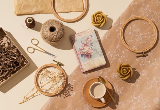Cup of coffee, sewing scissors, thread, jute, embroidery hoop, dry flowers, paper gift box, candles, old crumpled paper and vintage notebook on beige background. Minimal handmade accessories concept. photo