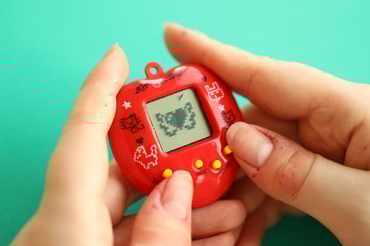 KYIV, UKRAINE - MARCH 9, 2024 Retro pet keychain game tamagotchi in red plastic case in female hands photo
