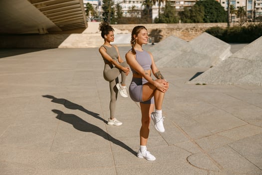 Two young sporty women in tracksuits are stretches legs outside on modern building background photo