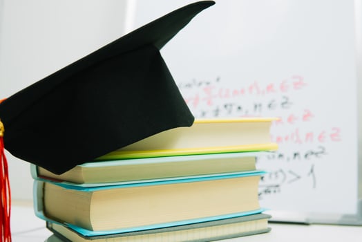 A black square graduate hat with a red tassel lies on a stack of books photo