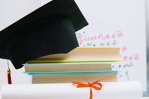 A black square graduate hat with a red tassel lies on a diploma and a stack of books. Education concept photo
