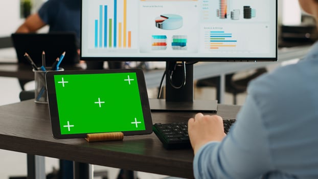Person using tablet with chromakey design on display, sitting at desk and analyzing product sales on computer. Company worker looking both at isolated mockup template and revenue network on pc. photo