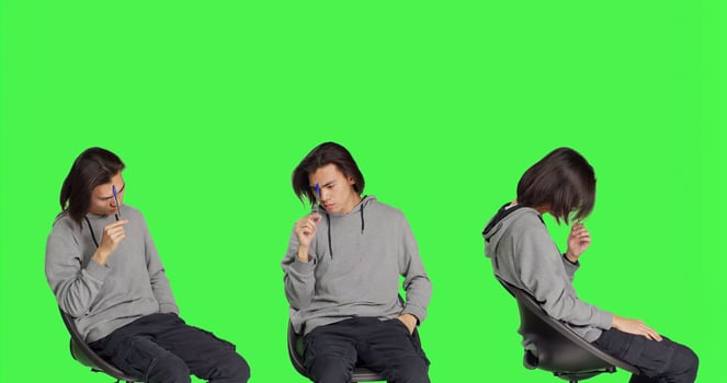 Male model thinking about solution over greenscreen backdrop, feeling uncertain about new dilemma. Asian man sitting on chair and acting confused, pensive thoughtful person. photo