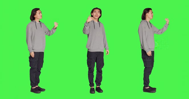 Asian man asking person to come over, encouraging people to get closer while he is standing against full body greenscreen. Adult in casual clothes urging someone to approach him. photo