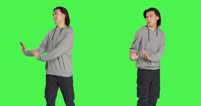 Male model pretending to push something aside, expressing rejection or refusal in studio. Young man mimicking dismissal over isolated greenscreen background, stop symbol. photo